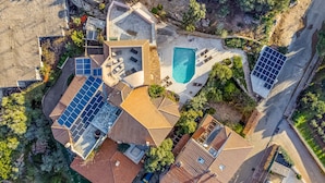 An aerial view of a residential property with multiple solar panels, a swimming pool, and a landscaped garden.