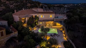 A Mediterranean-style villa with a swimming pool, outdoor seating, and a view of the surrounding landscape.
