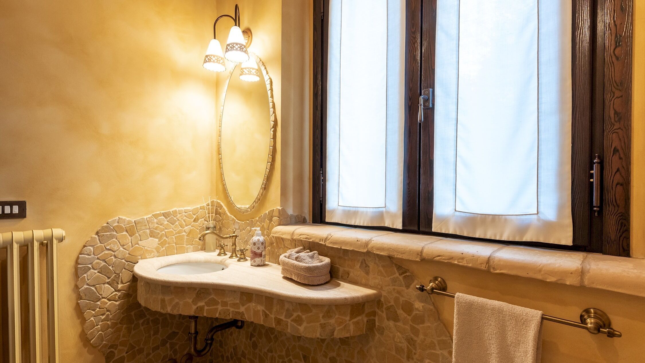 A bathroom with a stone sink, a mirror, a towel rack, and a window with curtains.