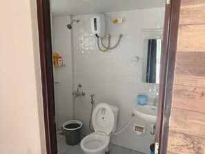 A small bathroom with a toilet, sink, and shower. There are toiletries on the wall and a bucket next to the toilet.