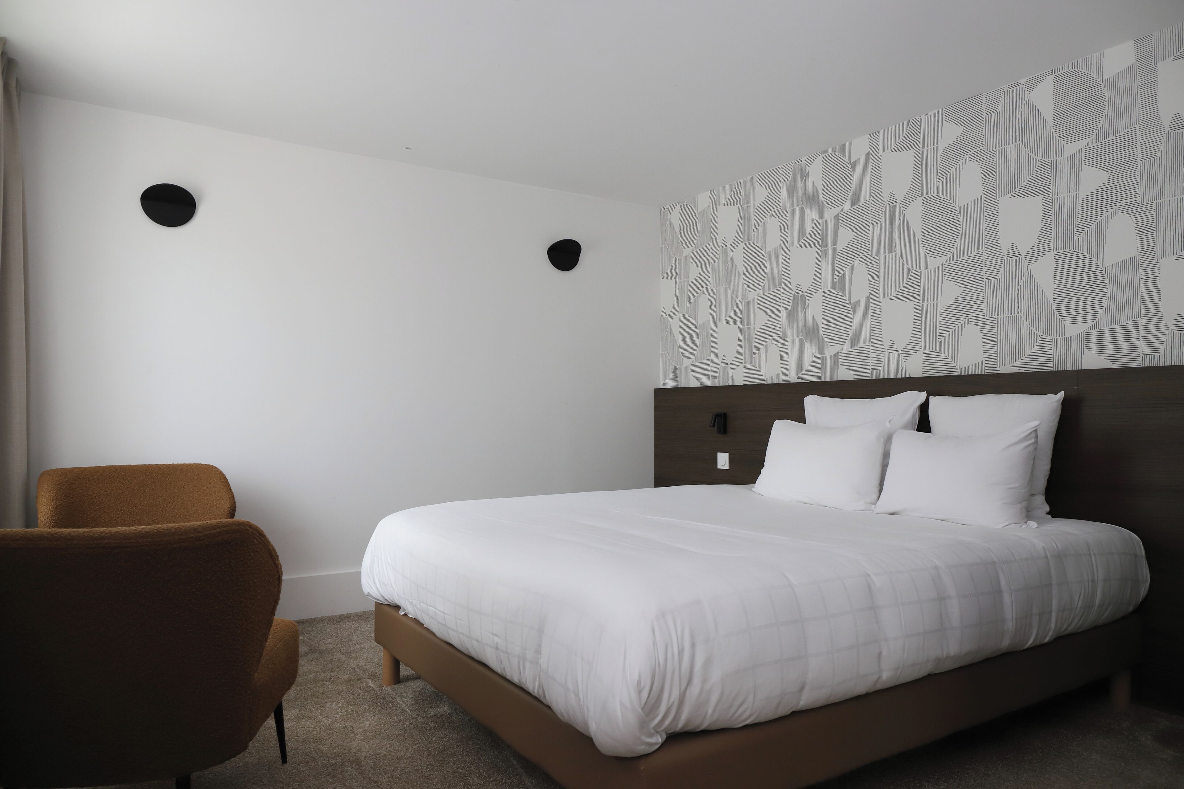 Una habitación de hotel con una cama grande, un sillón marrón y un papel tapiz estampado.