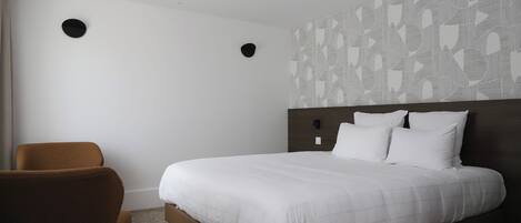 Una habitación de hotel con una cama grande, un sillón marrón y un papel tapiz estampado.