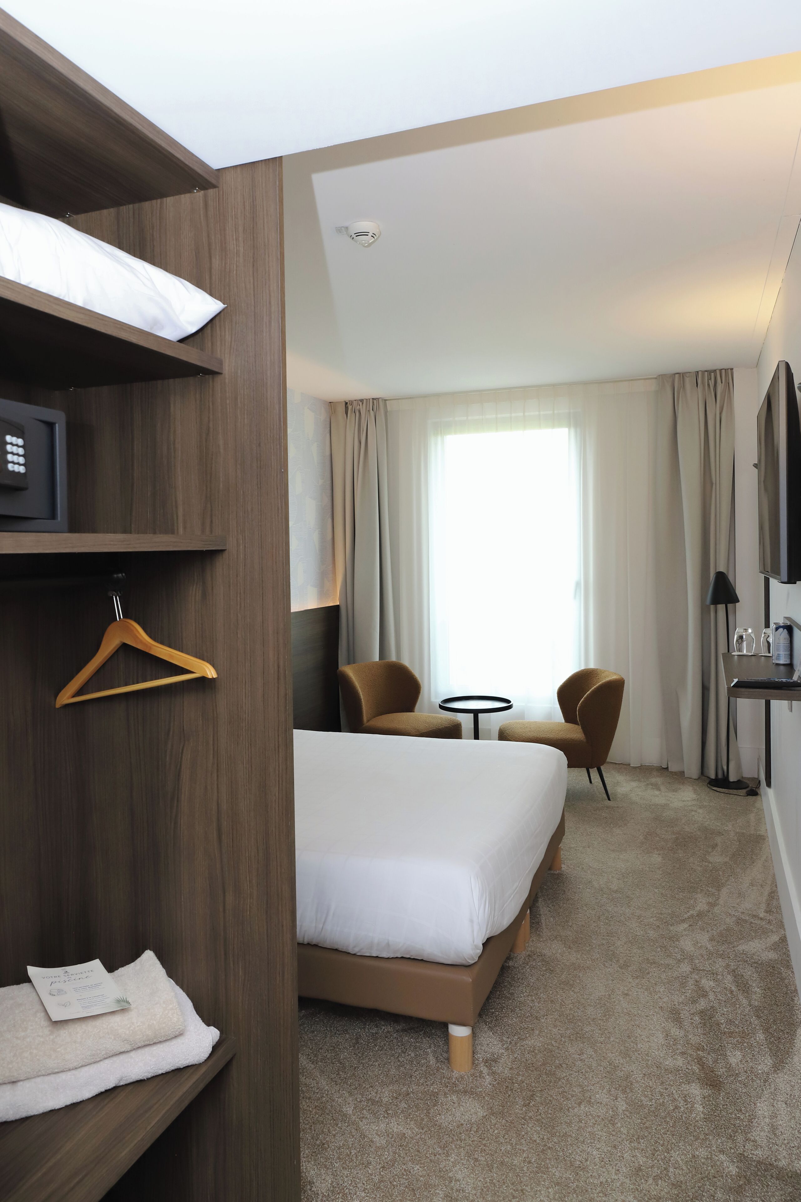 Une chambre d’hôtel comprenant un lit, deux fauteuils, une petite table, un téléviseur et une armoire.
