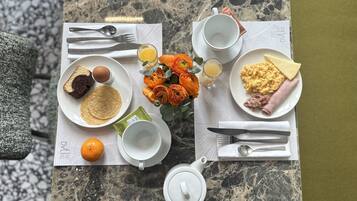 A breakfast table with plates of food, utensils, a teapot, and a vase of flowers.