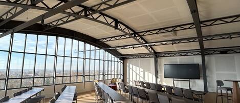 A conference room with long tables and chairs, large windows, and a high ceiling with metal beams.