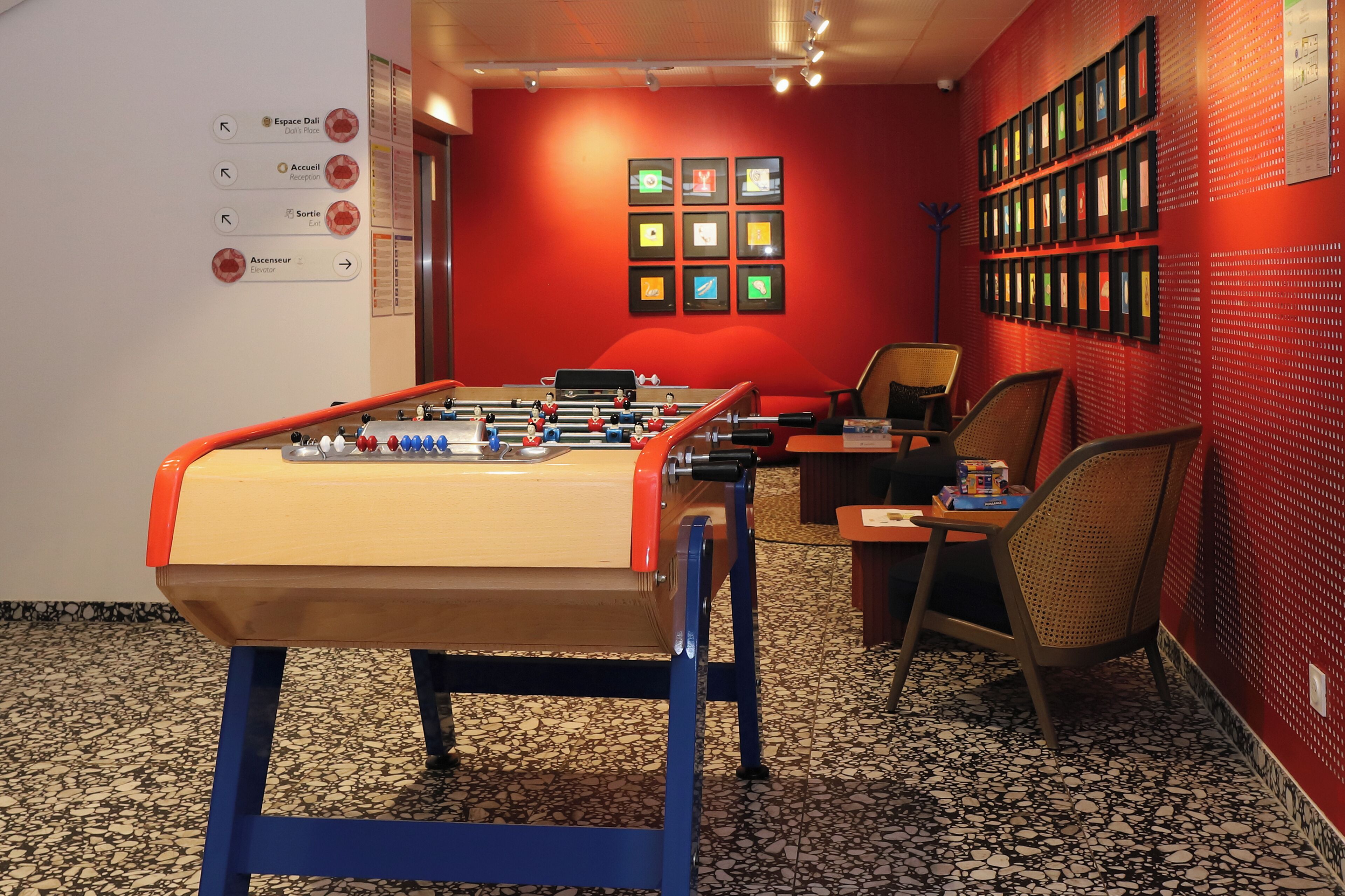 Une pièce comprenant une table de baby-foot, un comptoir d’accueil et un mur orné de tableaux.