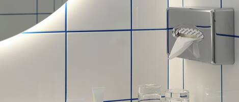 A bathroom with white tiles and blue lines, a hand soap dispenser, two glass containers, and a small wooden tray.