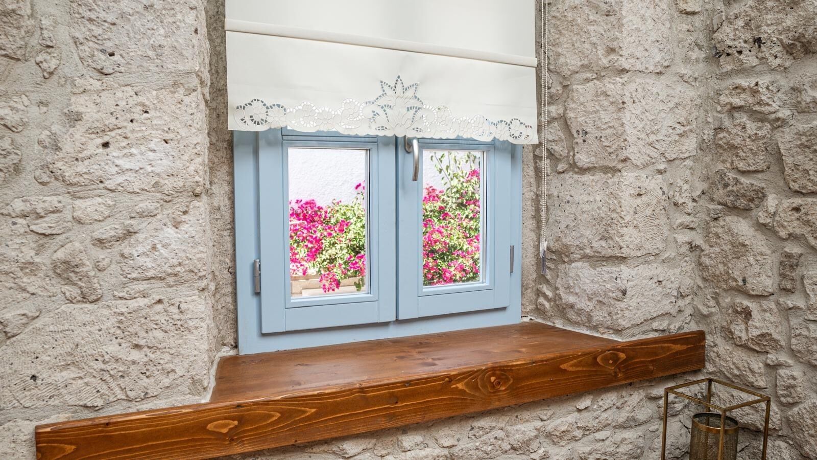Una ventana con encaje blanco en el marco y un estante de madera debajo.