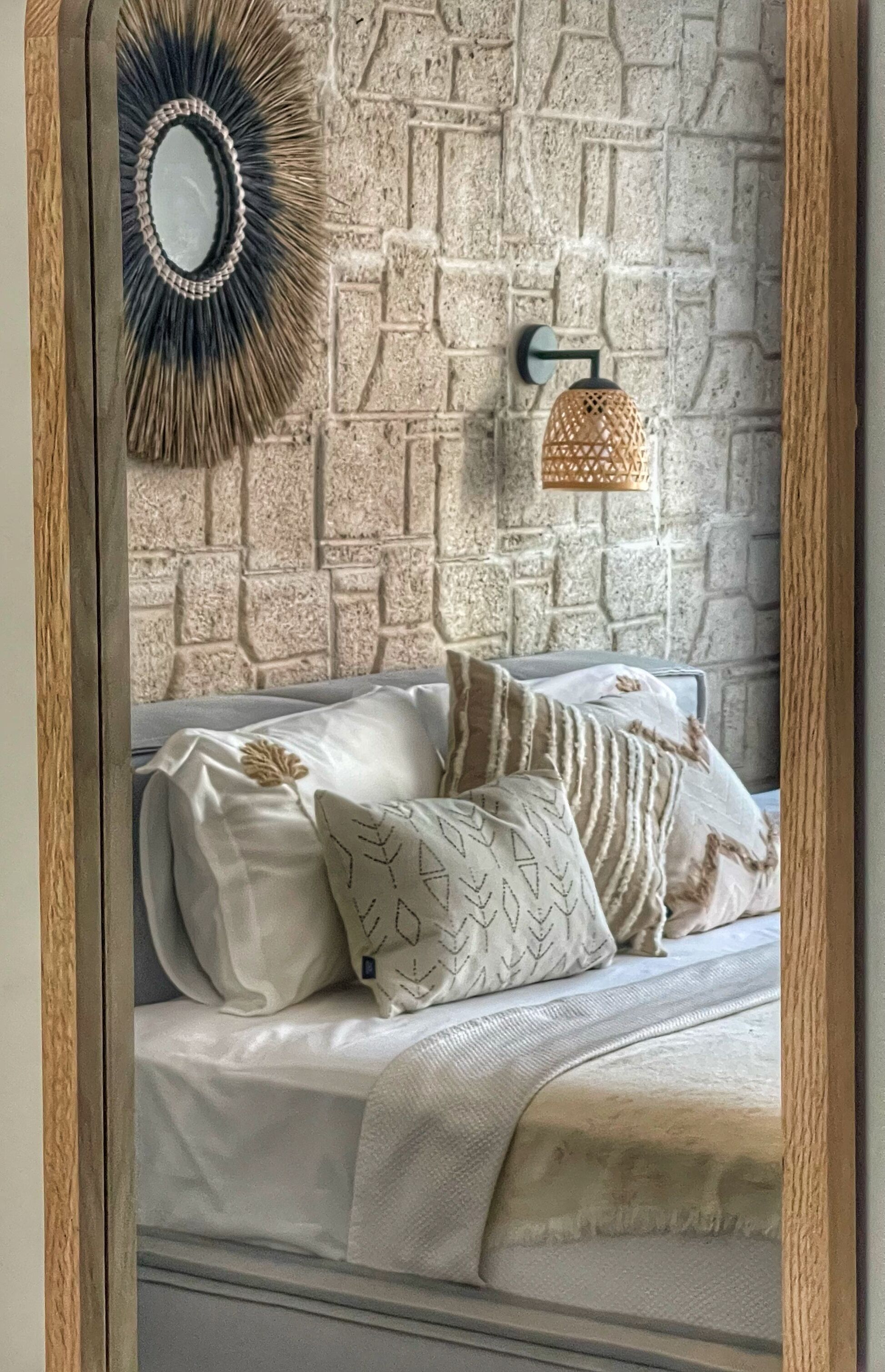 A bed with white bedding and patterned pillows against a textured stone wall.