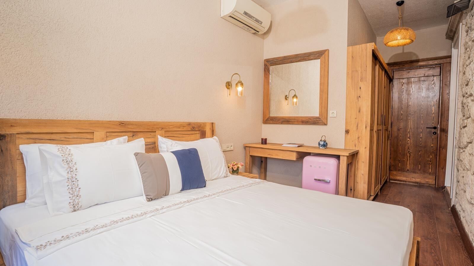 Ein Schlafzimmer mit einem Holzkopfteil, einem Nachttisch mit Spiegel, einem pinken Kühlschrank und einem Holzschrank.