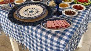 Una mesa dispuesta con diversos platos y bebidas, un jarrón con flores amarillas y un mantel a cuadros azul y blanco.
