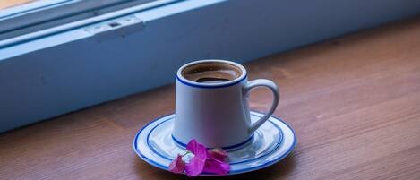 A cup of coffee on a saucer by a window with a blurred view of pink flowers outside.
