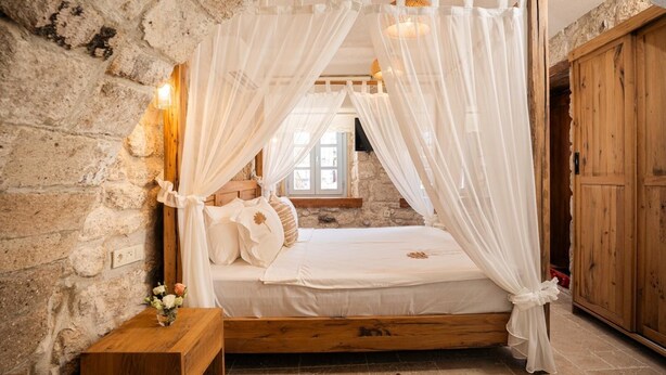 Un dormitorio rústico con pared de piedra, estructura de cama de madera y dosel.