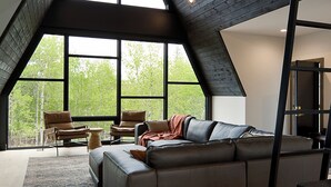 A spacious loft with a large sloped ceiling, a sectional sofa, and a view of trees through large windows. - One-of-a-Kind Double A Frame w/ Walkway, Windows Galore & Tons of Amenities! (Lead)