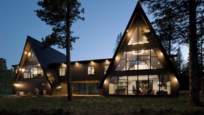 A modern, triangular-shaped house with large windows and a well-lit interior. - One-of-a-Kind Double A Frame w/ Walkway, Windows Galore & Tons of Amenities! (Lead)