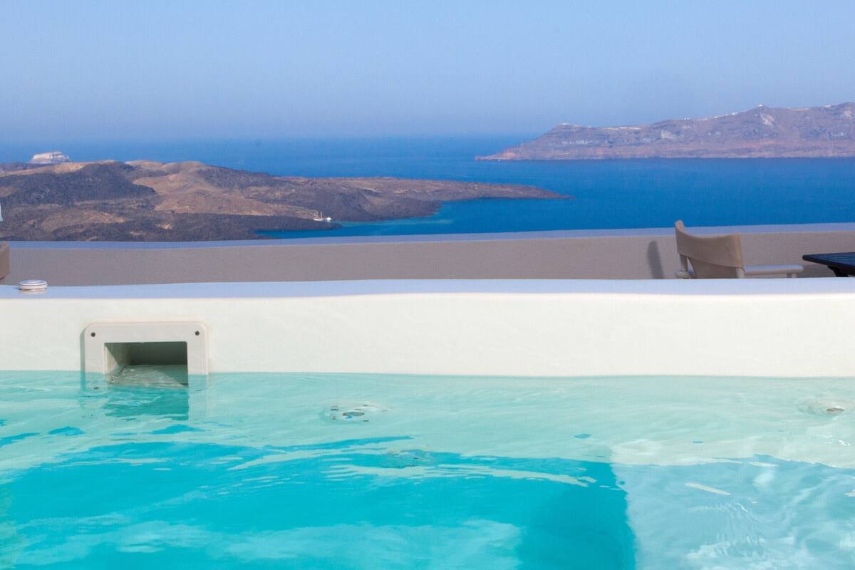 A pool with clear blue water, a chair, and a view of the sea and distant hills.