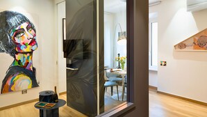 A modern interior with a glass partition, a dining area with a table and chairs, and a colorful abstract painting on the wall.