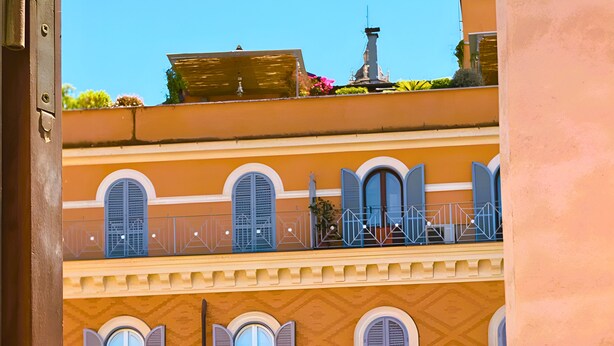 A balcony with wrought iron railings and a view of a building with multiple windows and balconies.