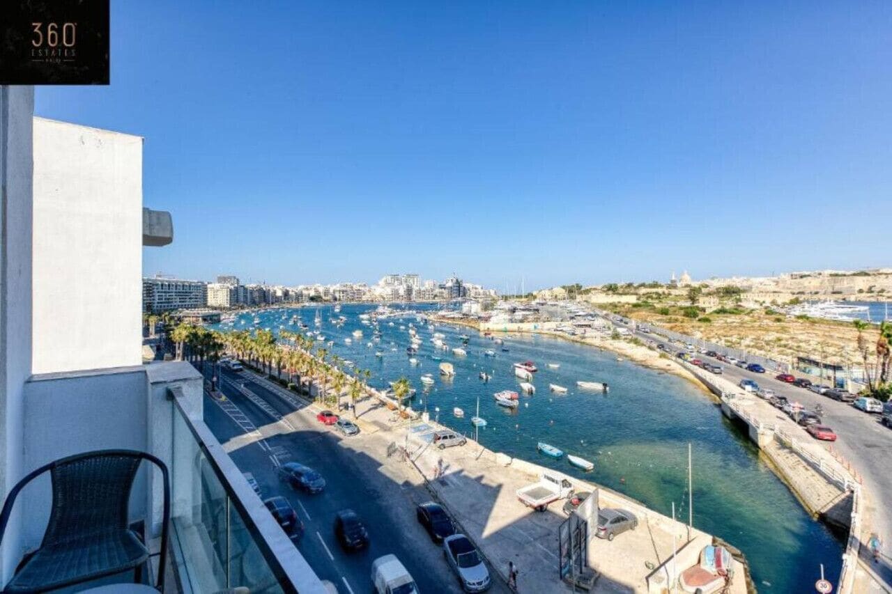 Un puerto deportivo con barcos, cielo despejado y un paisaje urbano al fondo.