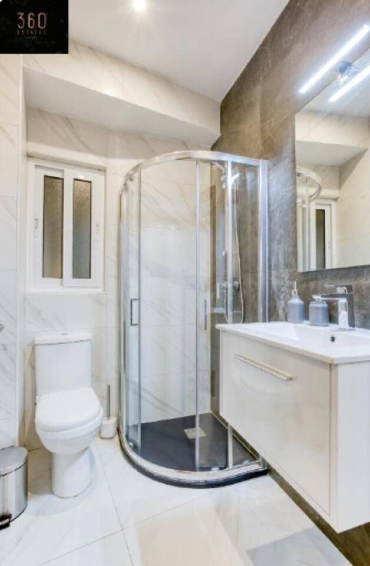 Un baño moderno con cabina de ducha de vidrio, inodoro y tocador con espejo.