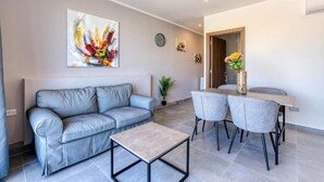 A modern living room with a grey sofa, a small coffee table, and a dining area with two chairs and a table.