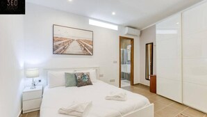 A modern bedroom with a large bed, a nightstand, a wall-mounted artwork, and a wardrobe.