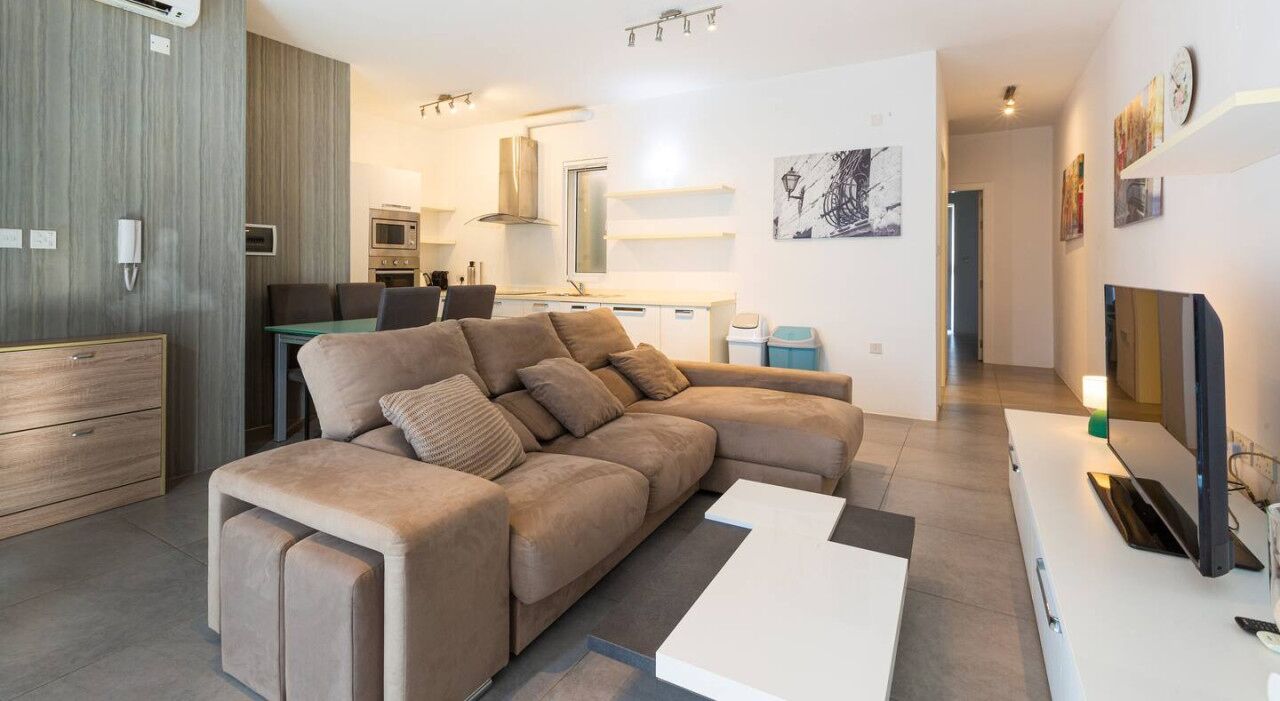 A modern living room with a sectional sofa, a dining area, and a kitchen in the background.