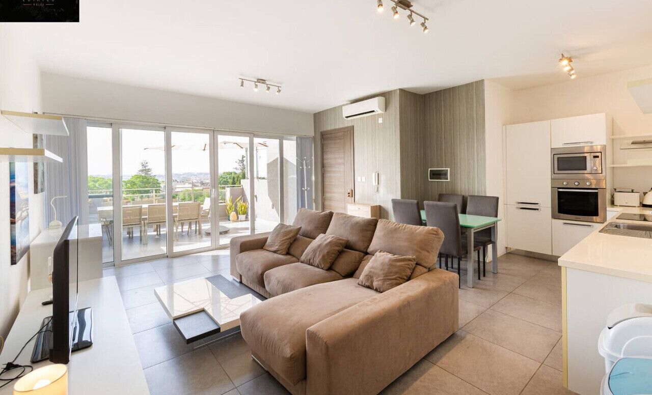 A modern living room with a sofa, a flat-screen TV, and a dining area with chairs.