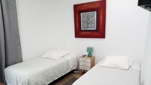 Una habitación con dos camas individuales, una mesita de noche con lámpara y un cuadro enmarcado en la pared.