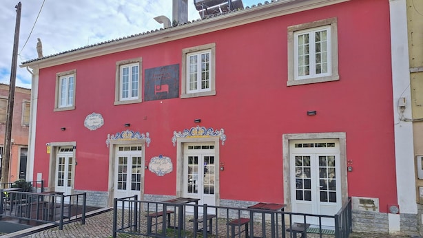 Un edificio rojo con múltiples ventanas, un balcón con mesas y sillas, y un cartel que indica un restaurante.
