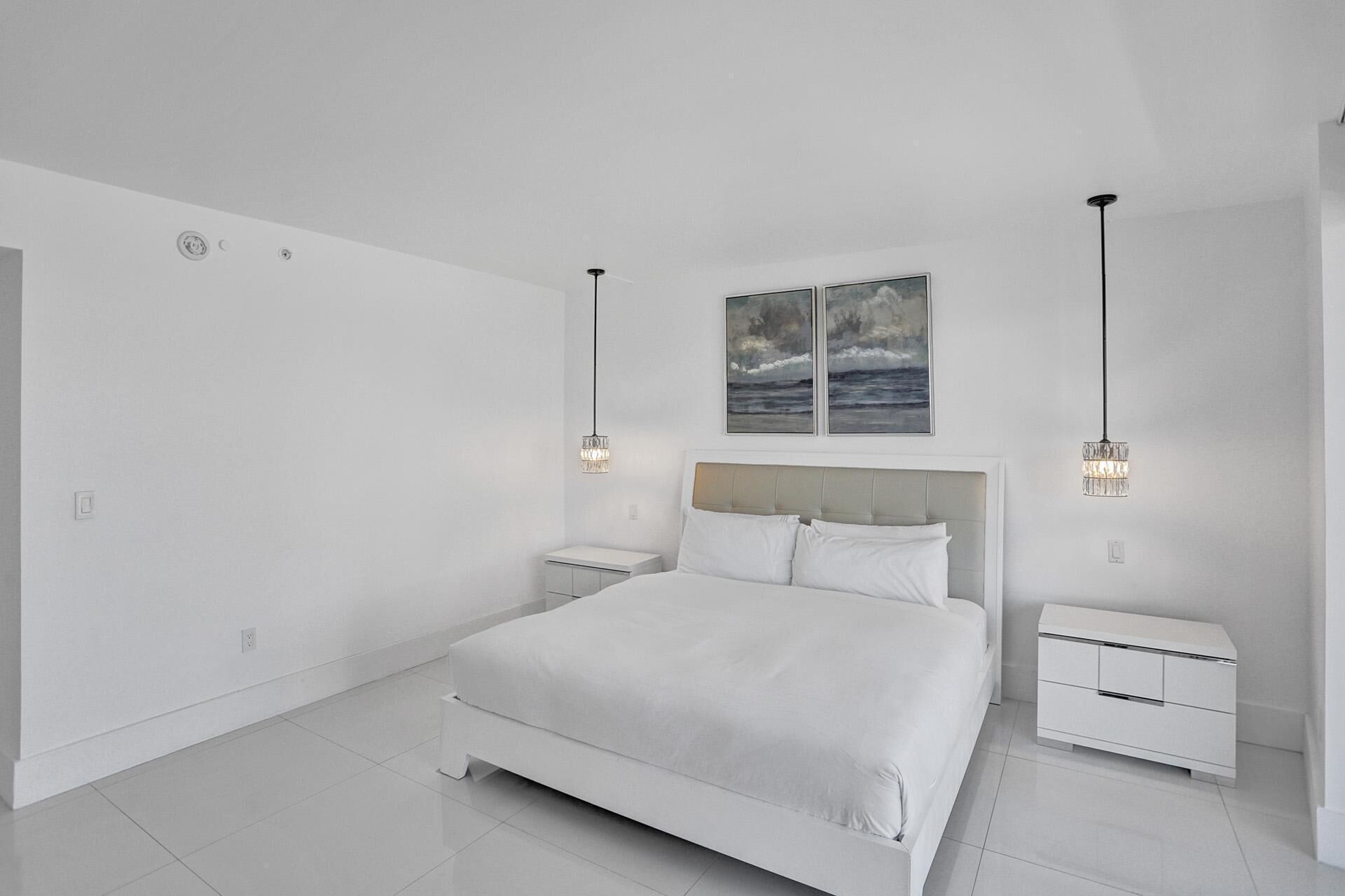 Un dormitorio minimalista con una cama grande, dos mesitas de noche y una obra de arte en el techo.