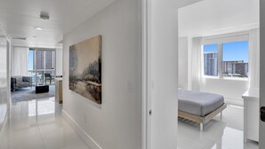 Ein modernes Hotelzimmer mit großem Fenster, einem Bett, einem Wandbild und Blick auf die Stadtlandschaft.