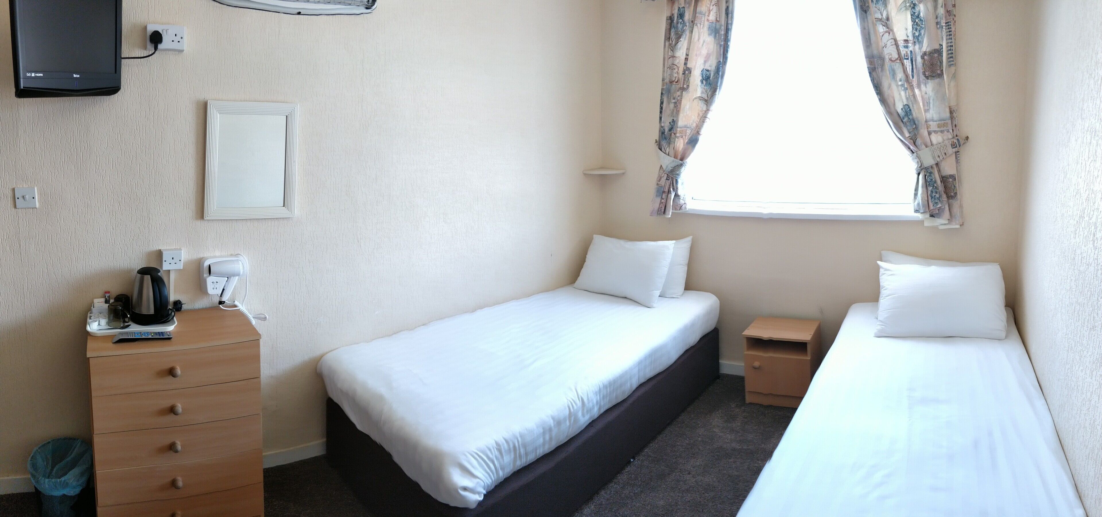 Una habitación de hotel con dos camas individuales, un aparador de madera, un televisor y una ventana con cortinas.