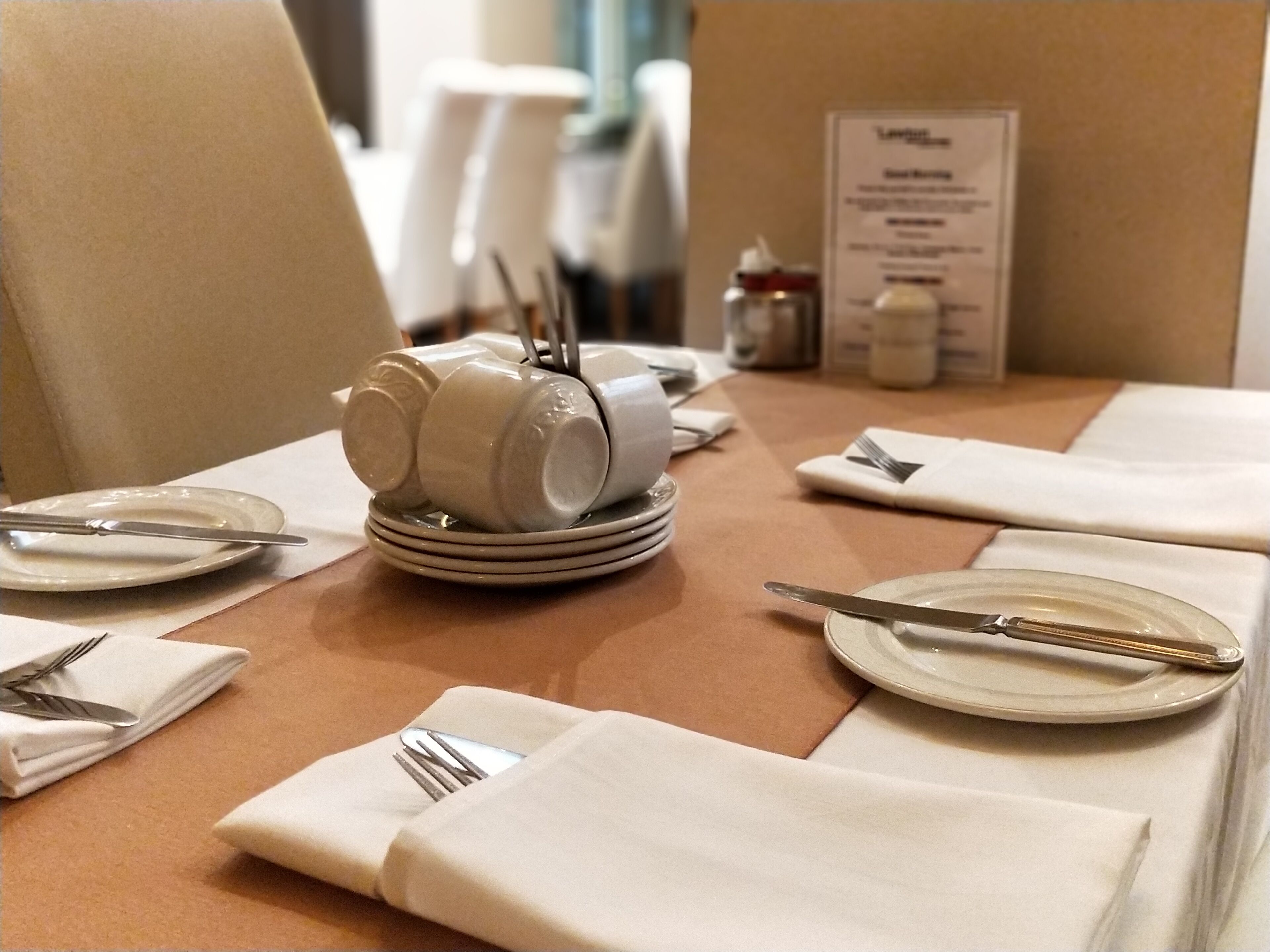 A neatly set dining table with plates, cutlery, and a stack of bowls.