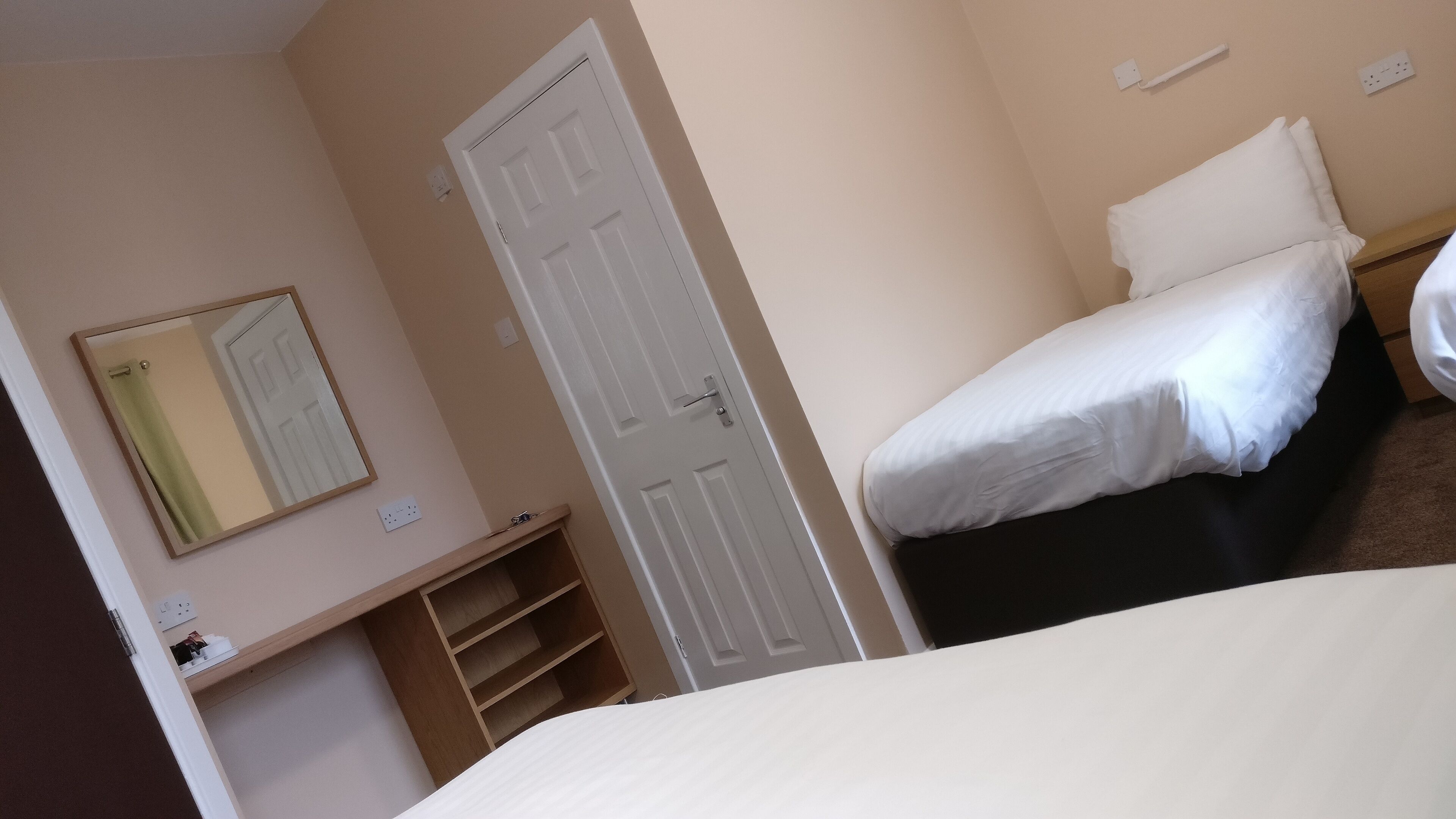 A bedroom with a bed, a door, a mirror, and a shelf with items.