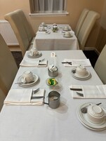 Een eettafel gedekt voor een maaltijd, met witte tafelkleden, genummerde placematen en netjes geordende bestek.