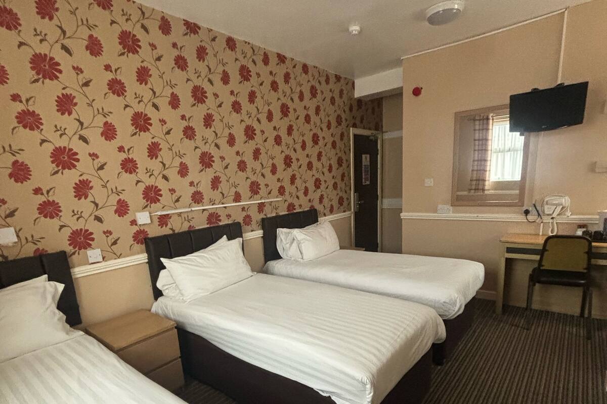 Une chambre d’hôtel avec trois lits, un bureau, une chaise, une télévision et une fenêtre avec un rideau.