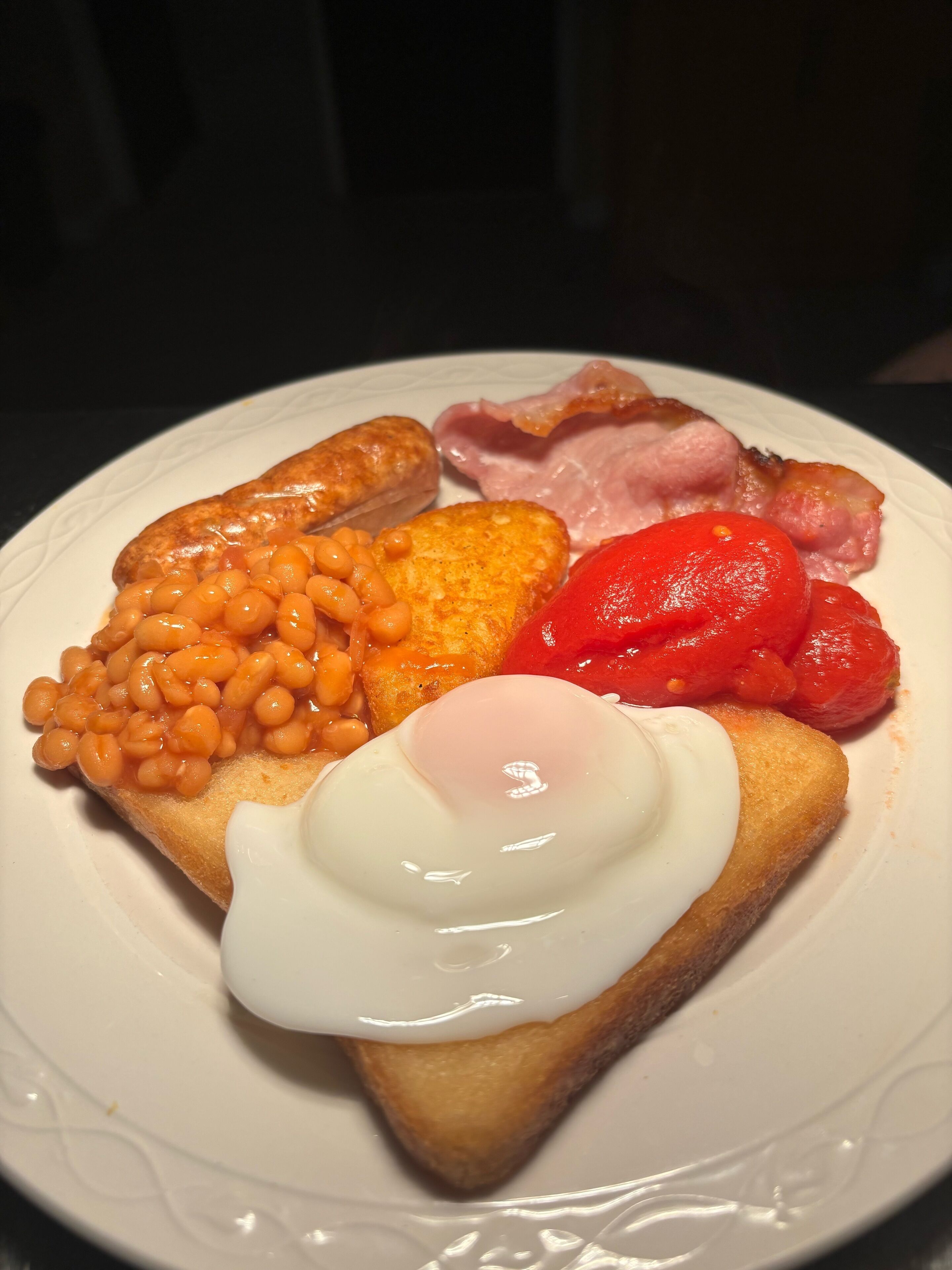 A plate of breakfast food including toast, eggs, beans, bacon, and tomatoes.