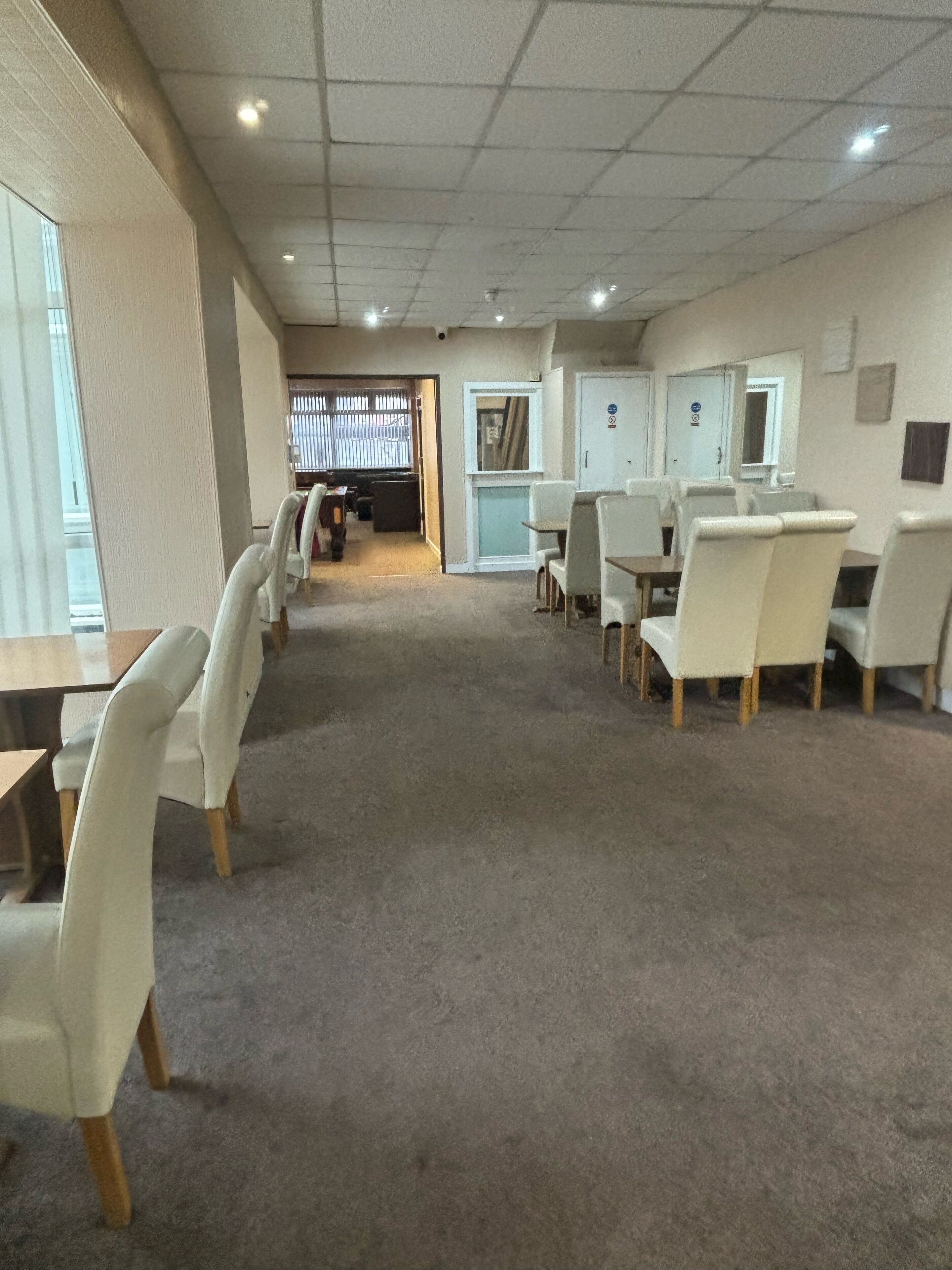 Un salón de conferencias con mesas y sillas, piso alfombrado y una puerta que da a otra habitación.