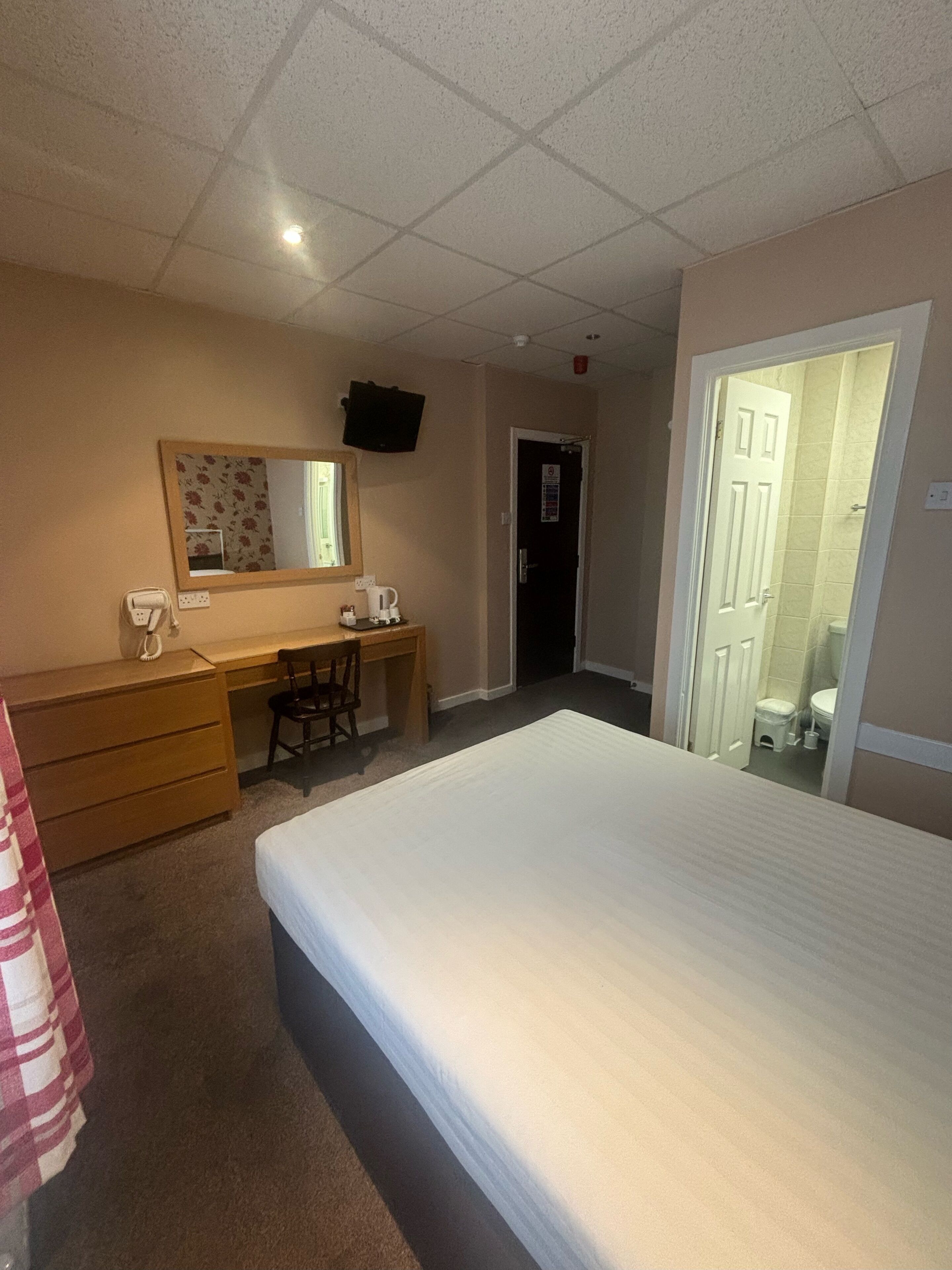 A hotel room with a bed, a desk, a chair, a mirror, and a door leading to a bathroom.