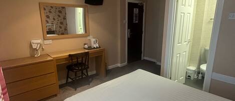 A hotel room with a bed, a desk, a chair, a mirror, and a door leading to a bathroom.