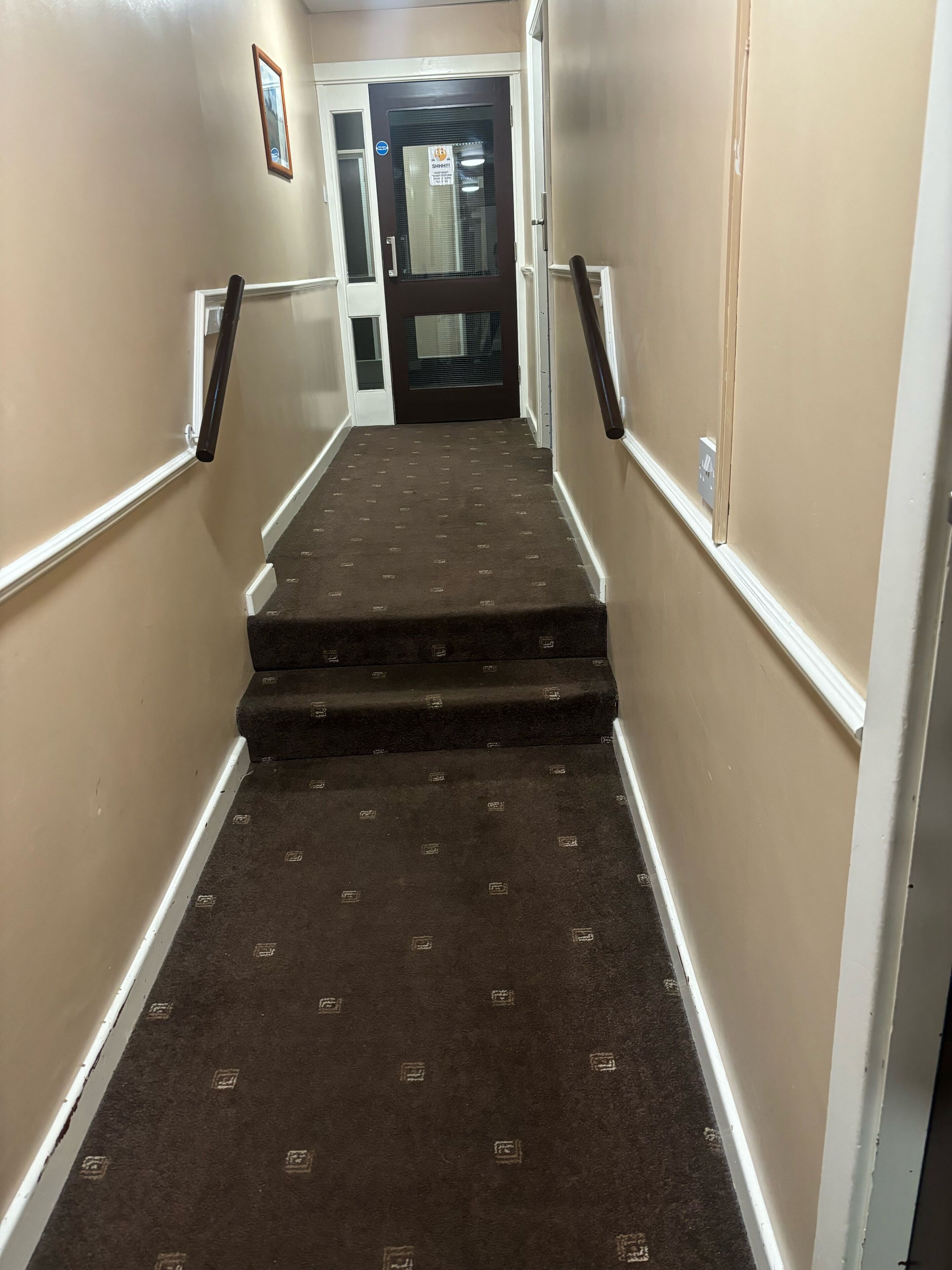 Una escalera alfombrada con barandilla que lleva a una puerta con un cartel.