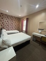 Een hotelkamer met twee bedden, een bureau met stoel, een radiator en een raam met gordijnen.