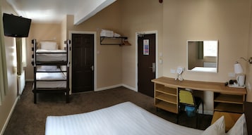 Een hotelkamer met stapelbedden, een bureau met een stoel, een spiegel, een telefoon en een radiator.