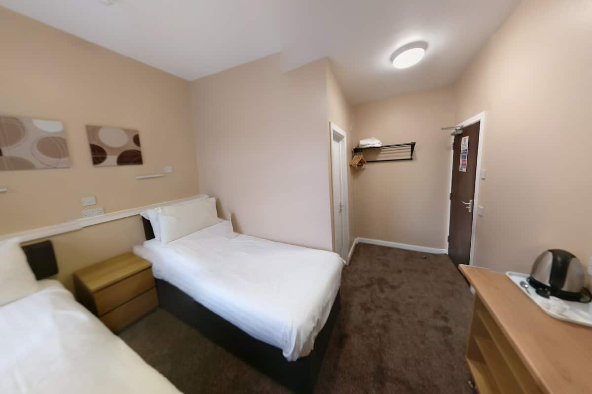 Une chambre d’hôtel avec un lit simple, une table de chevet en bois, un petit bureau et un porte-manteau.