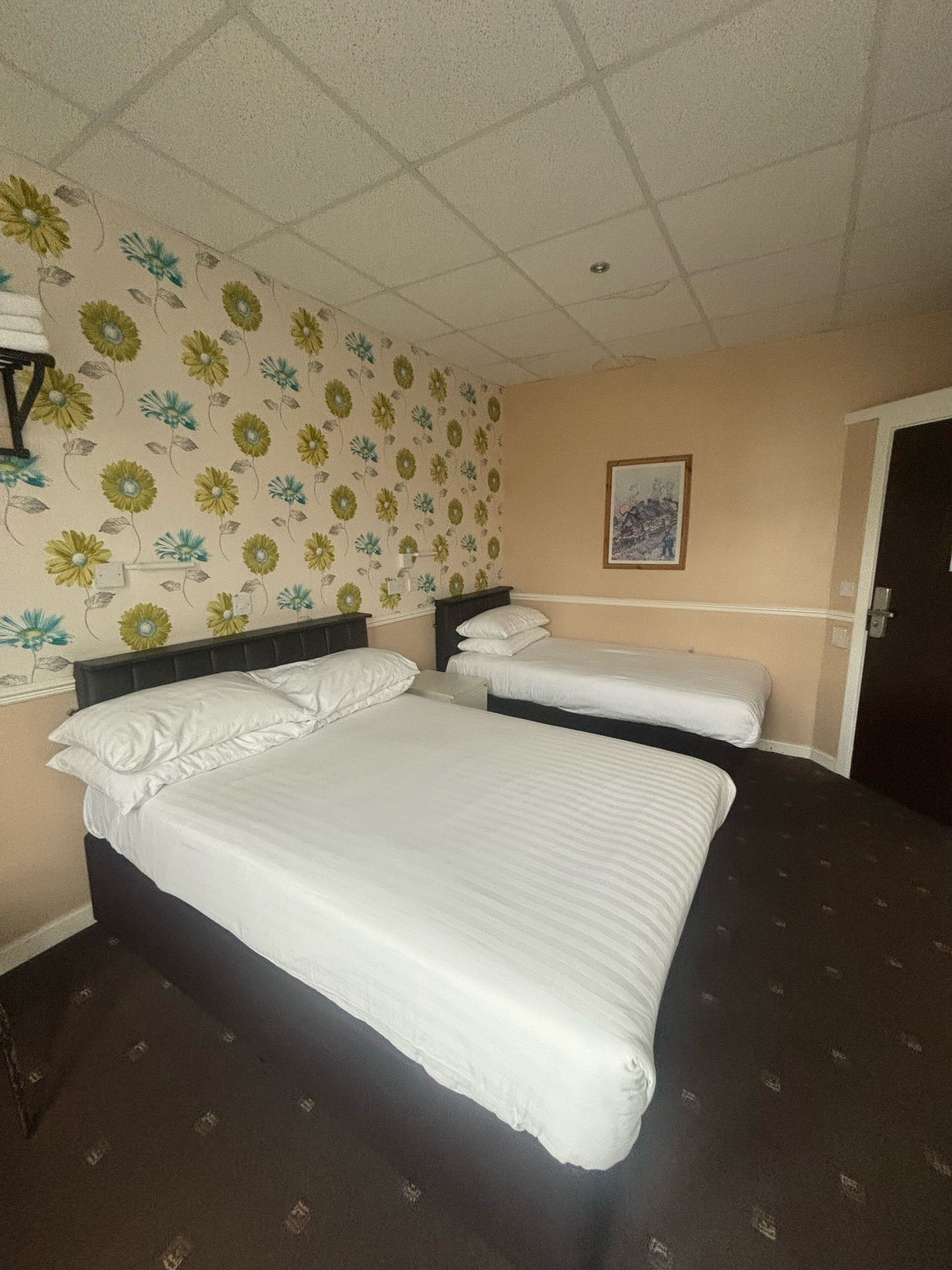 A hotel room with two beds, floral wallpaper, a framed picture on the wall, and a door.