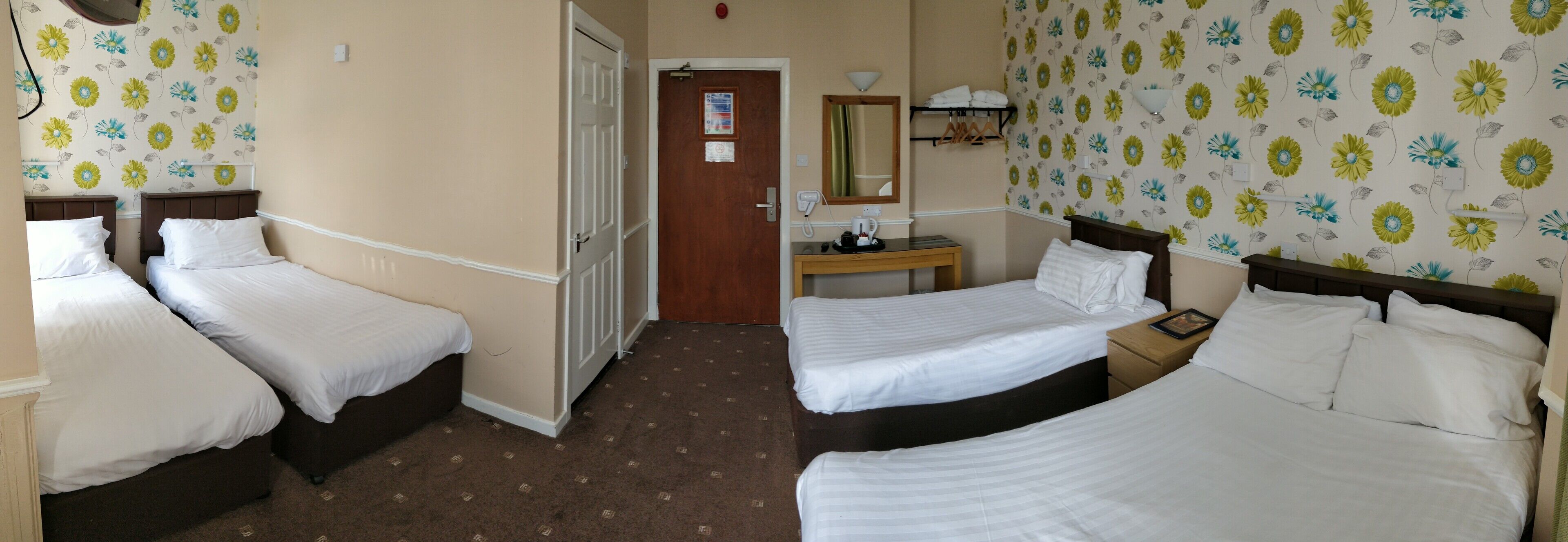 A hotel room with three single beds, a wooden nightstand, a mirror, and a door leading to another room.