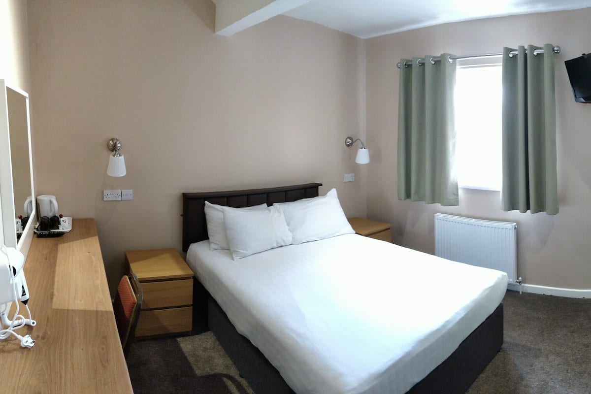 Une chambre d’hôtel avec un lit simple, un bureau avec une chaise, un radiateur, une fenêtre avec des rideaux et un lit superposé.