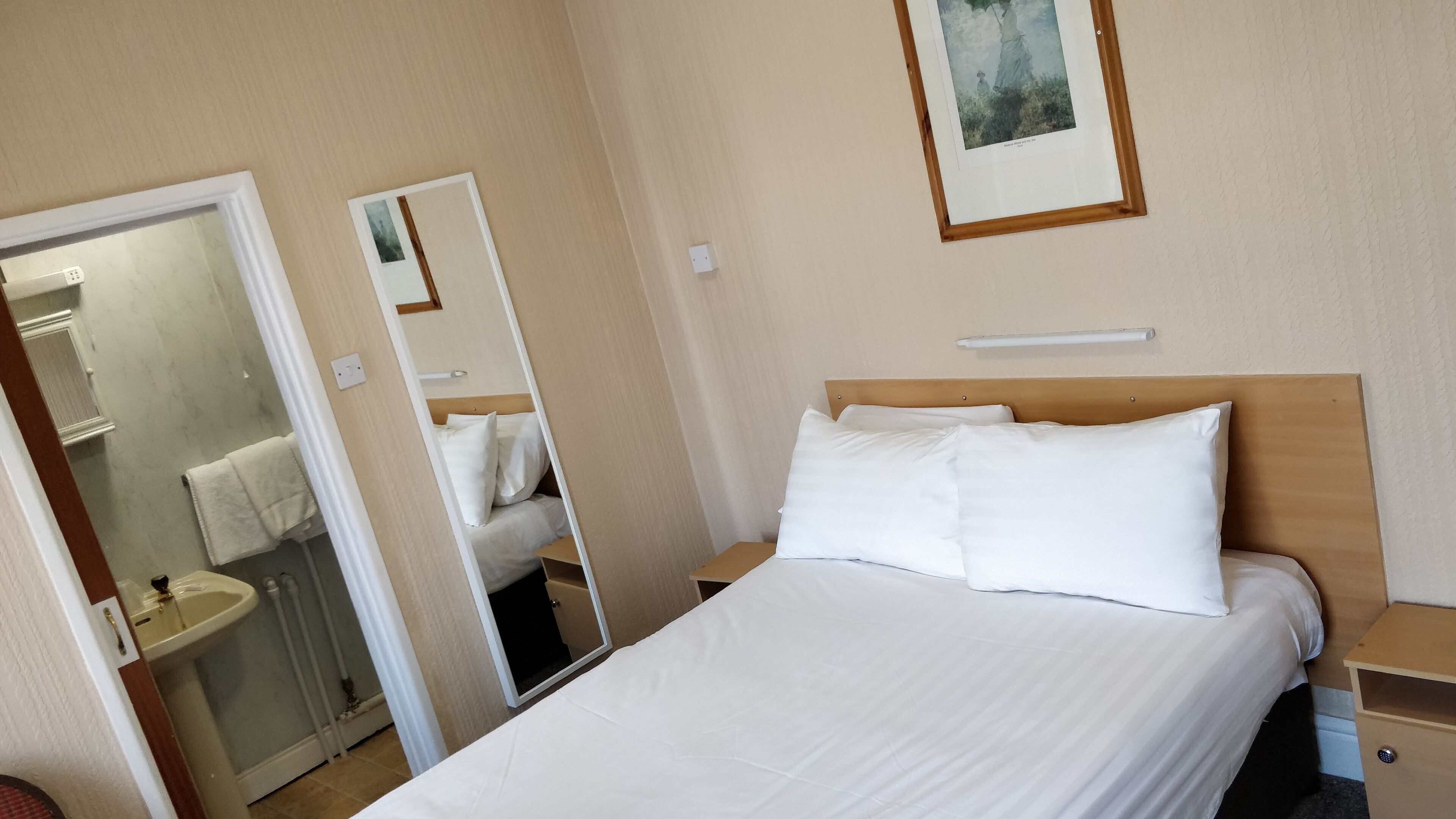 Een hotelkamer met een bed, nachtkastje, spiegel, wastafel en een handdoek aan de muur.
