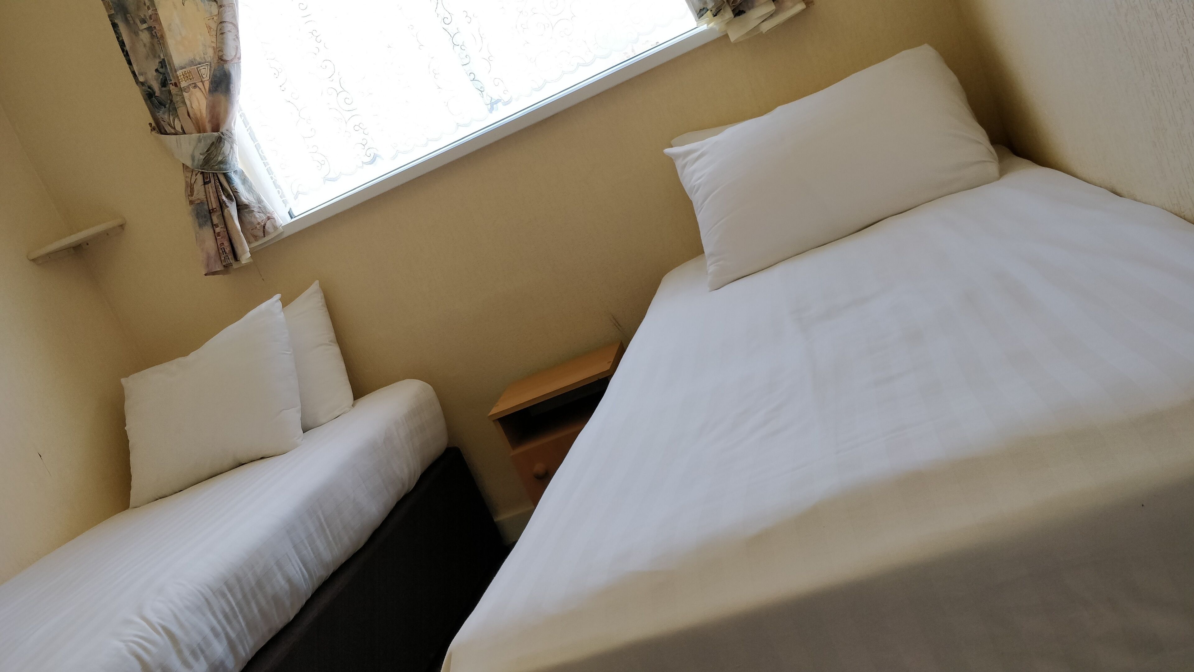 A room with two beds, a window with curtains, and a small wooden nightstand.